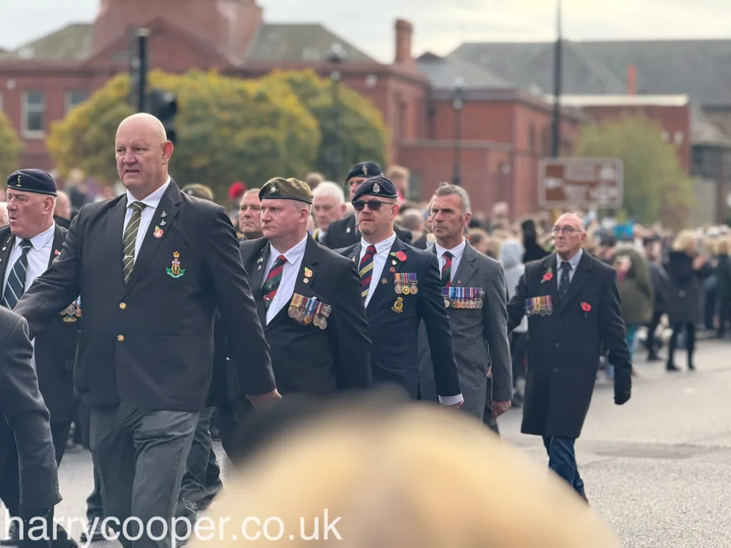 Veterans, many adorned with medals and wearing black blazers and berets, march together as part of the Remembrance Day parade, honouring their service and fallen comrades.