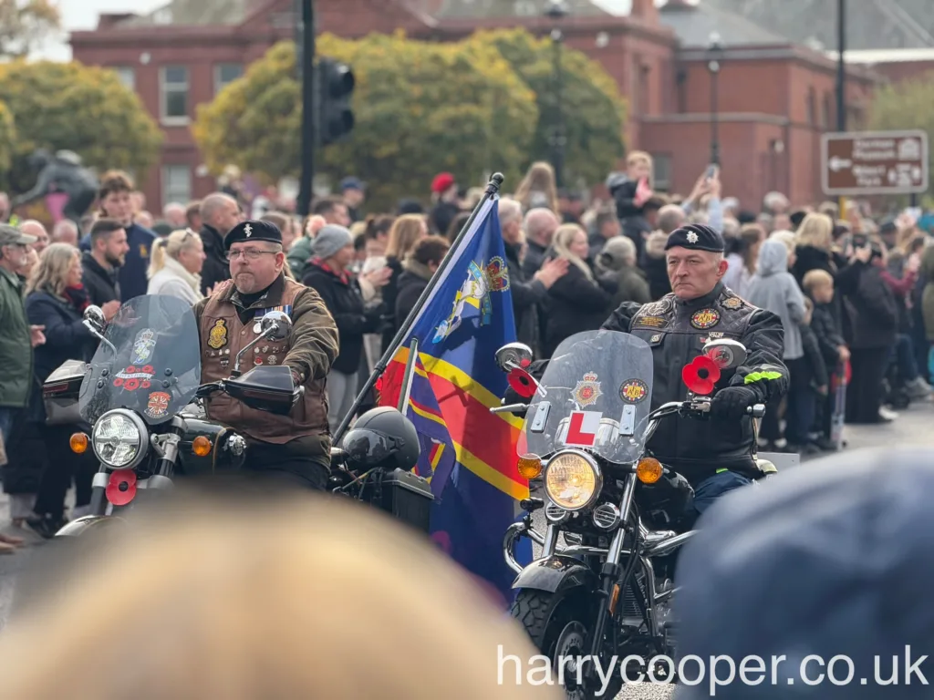 Two veterans on motorcycles decorated with flags and poppies, leading a section of riders in a remembrance day procession.