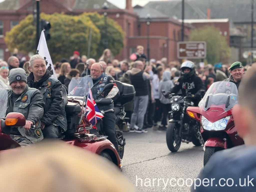 Several motorcyclists, including one with a Union Jack flag and a man in a green beret, ride motorcycles as part of the remembrance day events.