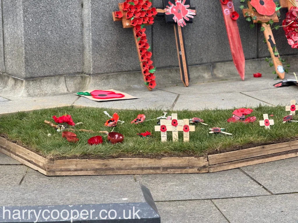 A small patch of grass at the cenotaph is adorned with poppy crosses and red poppies, each representing an individual remembrance tribute.