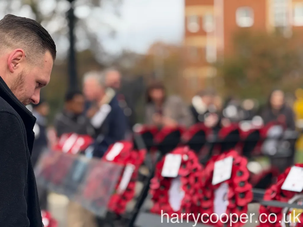 A young man stands with his head bowed, looking at rows of red poppy wreaths placed in honour of fallen soldiers.